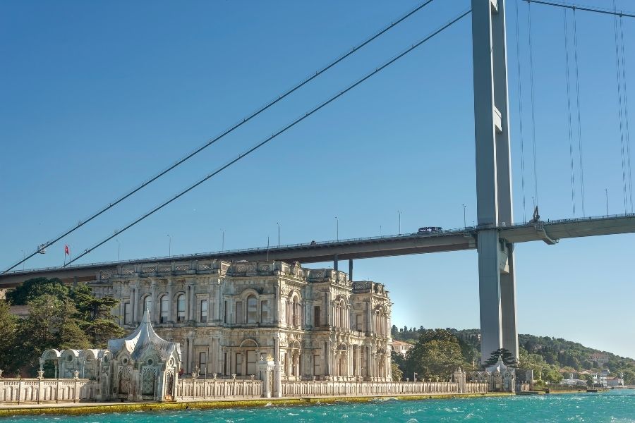 Beylerbeyi Palace on the Bosphorus in Istanbul, positioned beneath the Bosphorus Bridge, with clear skies and turquoise water.