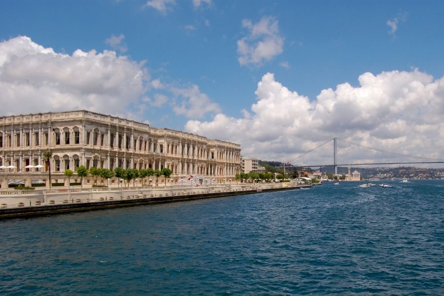 Çırağan Palace on the Bosphorus in Istanbul, with its grand facade, waterfront setting, and Bosphorus Bridge in the background.